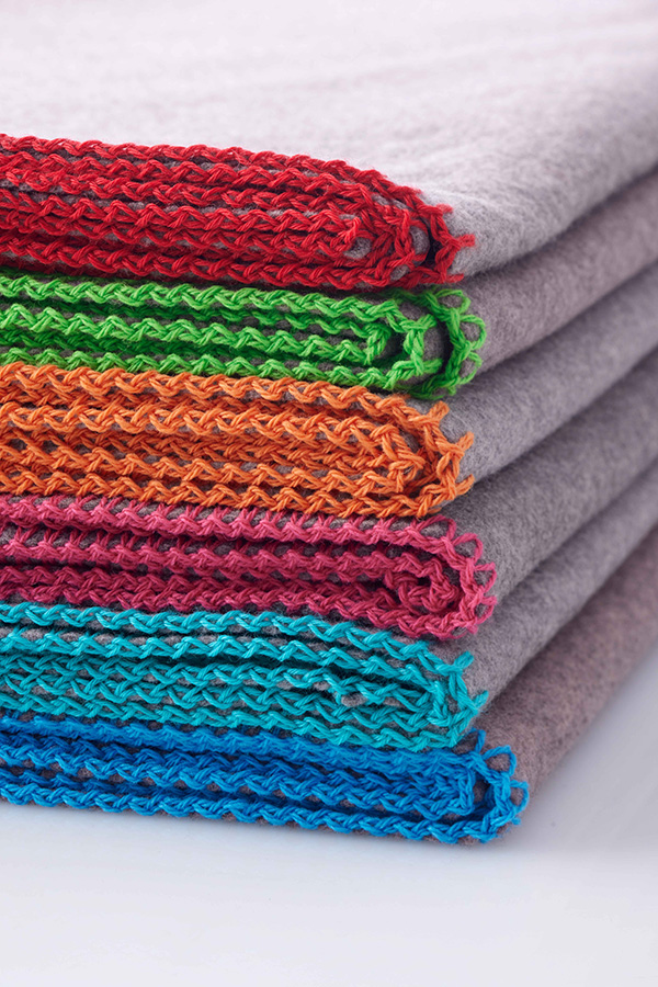 Sechs gefaltete graue Decken mit roten, grünen, orangen, pinken, türkisen und blauen Kanten