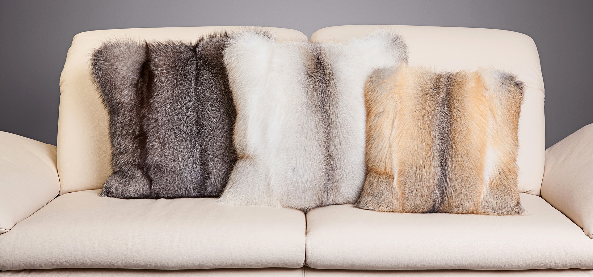 Drei Fellkissen in Grau, Weiß und Beige auf einem hellen Sofa