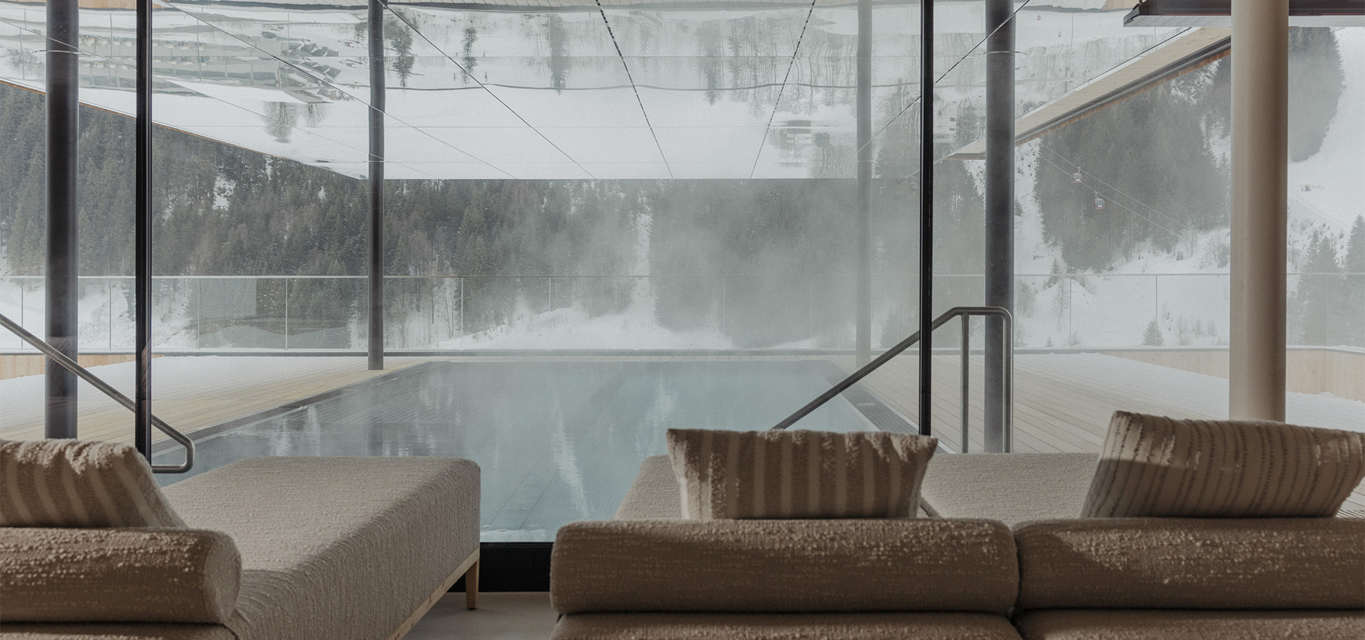Pool mit Liegen hinter einer Glasfront, draußen verschneite Bäume
